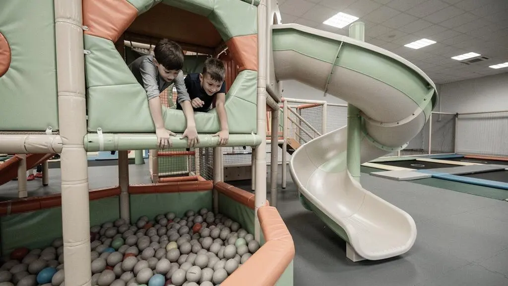 Deux enfants grimpent dans une structure de jeux couverte multi-niveaux d'un parc indoor.